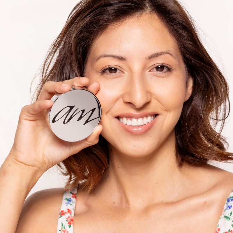 A woman holding up a canister with the letters 'AM' on it indicating an Advanced Mineral Makeup product.