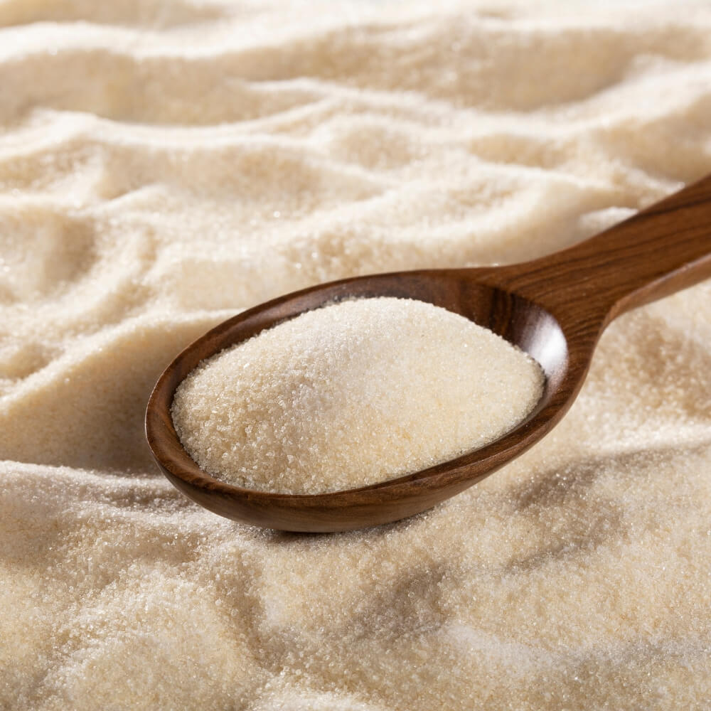 A wooden spoon filled with off white powder sitting in a pile of the same powder.