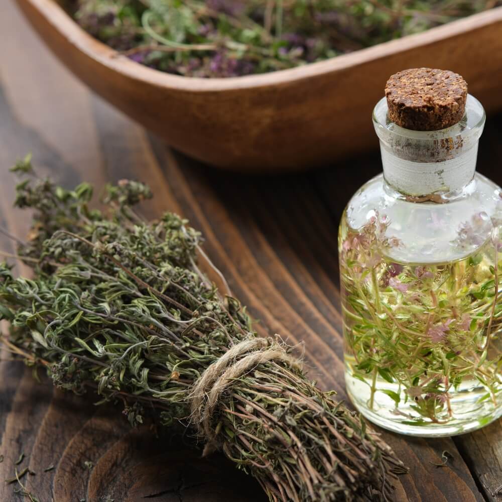 A small jar with liquid and the herb Thyme in it next to a bowl and a bundle of dried Thyme.